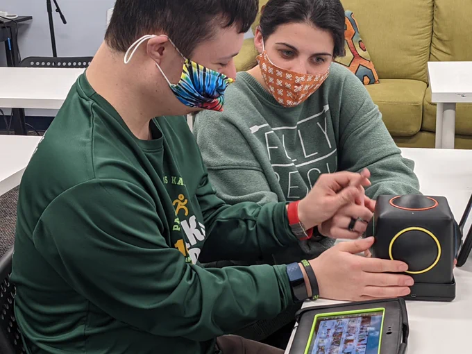 Young man playing the Skoog with a female instructor assisting. 