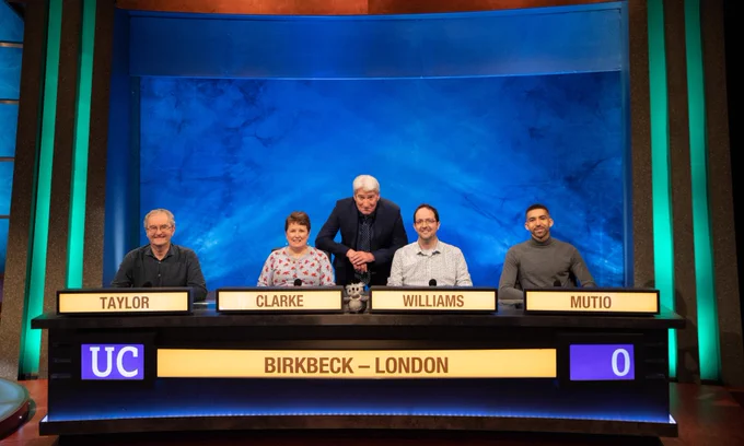 The University Challenge Birkbeck team on the show, smiling for the camera with Jeremy Paxman stood behind them.