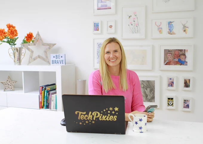Joy Foster founder of TechPixies smiling, seated at her office desk with a laptop