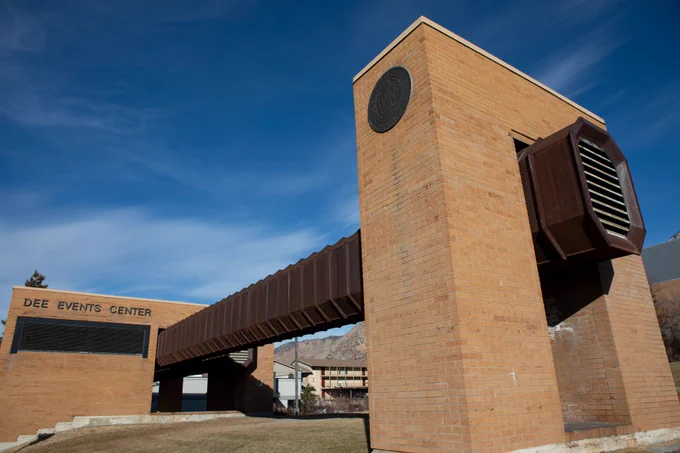 A photo of the Dee Events Center marquee and arts feature. The feature is made of two brick structure and has a brown metal duct running between each structure.