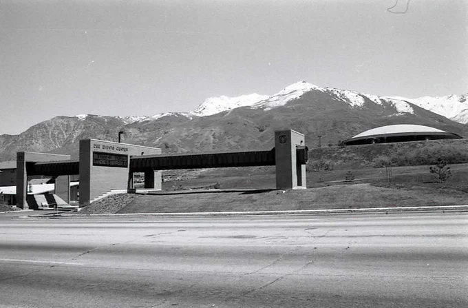 A historic, black and white photo of the Dee Events Center art feature and marquee, shot from the opposite side of Harrison Boulevard. The Dee Events Center dome is visible in the background, as are the Wasatch Mountains. 