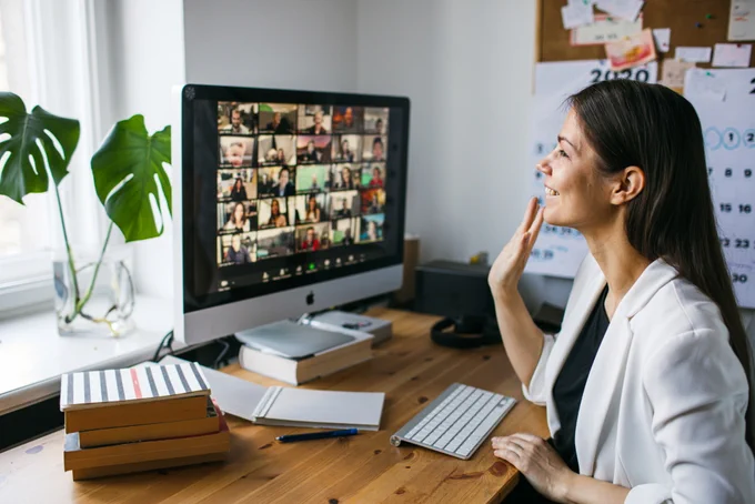 Image of a woman engaged in online learning, waving at a computer on which icons of people's faces can be seen