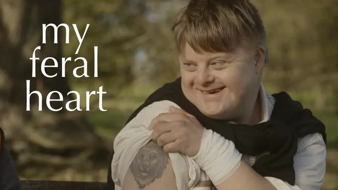 A photo from the film 'My Feral Heart' showing lead actor Steven Brandon showing a tattoo of a lion on his upper shoulder. Steven has Down's syndrome and is smiling. 