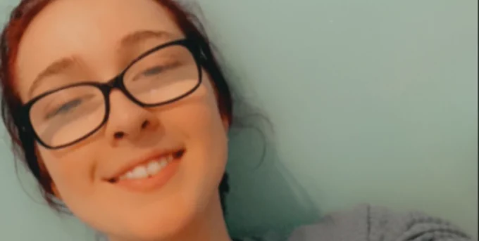 A close up of Annie-Rose smiling to camera. She is wearing glasses.