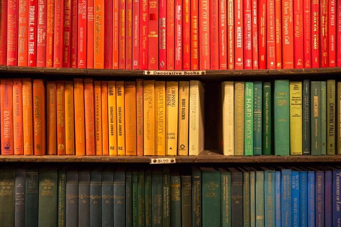 Three shelves of books, arranged by colour, with one book missing, creating a hole in the display. 