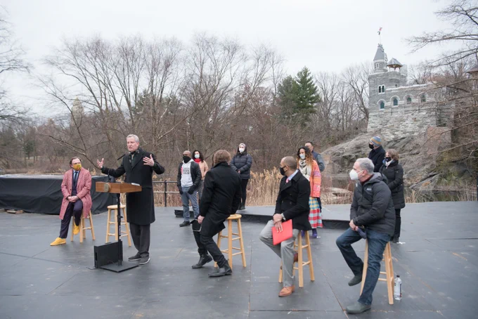 A photo of the Mayor and others seated on stools on an outdoor stage with a small castle rising behind them.