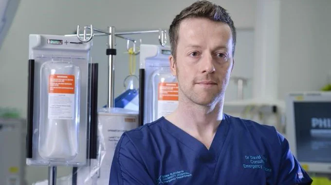 Dr David Lowe, standing in front of monitors and drip. Photo taken from chest height.