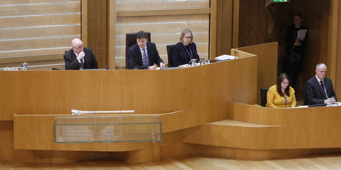 Presiding Officer Ken Macintosh, flanked by clerks to either side.