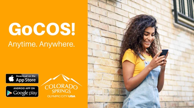 young woman leaning on exterior brick wall as she texts. GoCOS! anytime, Anywhere. apple app logo. Google play logo. City logo.