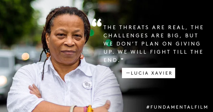 Text: "The threats are real, the challenges are big, but we don't plan on giving up. We will fight til the end." Lúcia Xavier
Image: Lúcia stands with her arms crossed and a smile on her face.