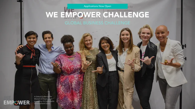 Text: Applications now open: We Empower Challenge. Global Business Challenge. Logo: We Empower. A global challenge for women entrepreneurs powering UN Sustainable Development Goals. Background: a photo of a group of eight ethnically diverse women at a We Empower event, all giving the “hang loose” hand sign. 