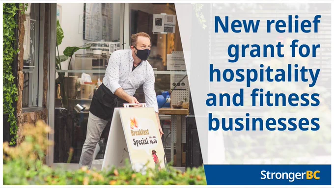 An employee sets up a sandwich board outside a restaurant. Text reads: New relief grant for hospitality and fitness businesses.