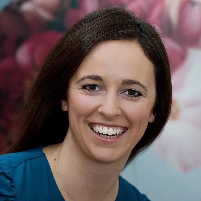A white woman with dark hair and blue shirt smiling. 