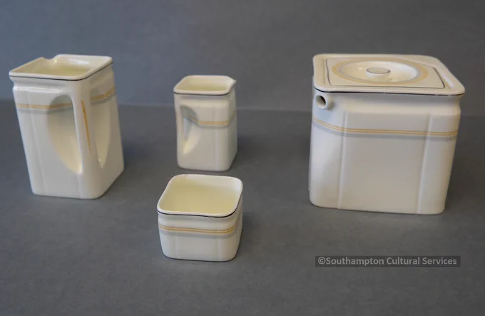 Square tea set, with milk jug, tea pot, cream jug and sugar bowl. All are made of cream ceramic and have an orange and grey band running around the top part of the jug or bowl.