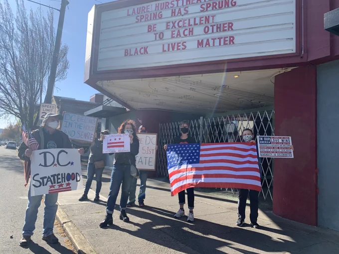 People stand outside the Laurelhurst Theater on E Burnside with signs supporting DC statehood and a 51-star flag