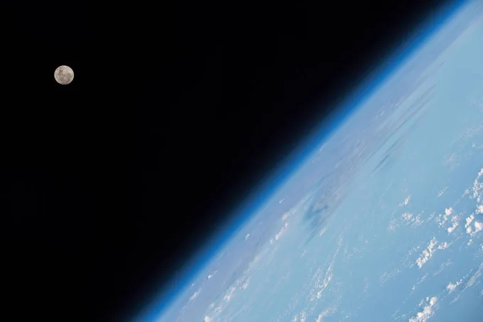 Moon in the distance and Earth's horizon at an angle photographed from low-Earth orbit aboard the International Space Station
