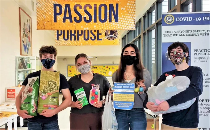 Students in a school hallway hold some of the pet supplies they collected. 