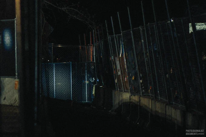 Friday, April 16th, 2021: A bright light shines down through the fences onto a protester that breaches the first barricade surrounding the Brooklyn Center Police Department to hang a green air-freshener on a secondary fence. Shortly after this photo was captured, a flash-bang detonates in the moat inches away and then Unlawful Assembly is declared over a loud speaker. Air-fresheners have been used as a symbol protesting the death of Daunte Wright who was shot by Brooklyn Center police officer Kim Potter Sunday, April 11th.
