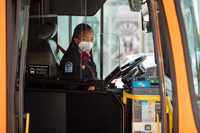 photo taken through the front door of a bus of young black female bus operator behind the wheel
