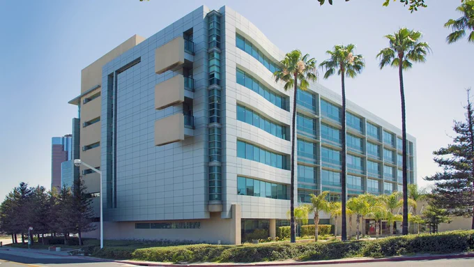 A large metal and glass building with palm trees in front of it.