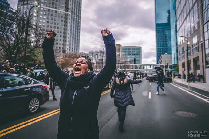 Both fists raised in the air, a woman yells in celebration while walking down the street outside of the Hennepin County Courthouse  (04/20/2021) photo by @pjdocs