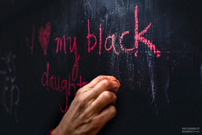 A mother, who is white, grabs a piece of bright pink chalk and writes on the black-painted plywood wrapping around the sides of U.S. Bank Plaza across from the Hennepin County Courthouse; her message reads "I [heart] my black daughter!!" (04/20/2021 - photo by @pjdocs) 