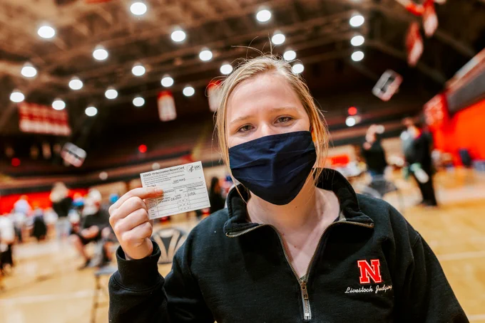 A student holds up their vaccination card at the Coliseum after receiving their first shot