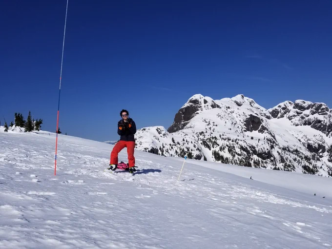 Scientific researcher standing on a mountaintop in snow with a probe measuring depth