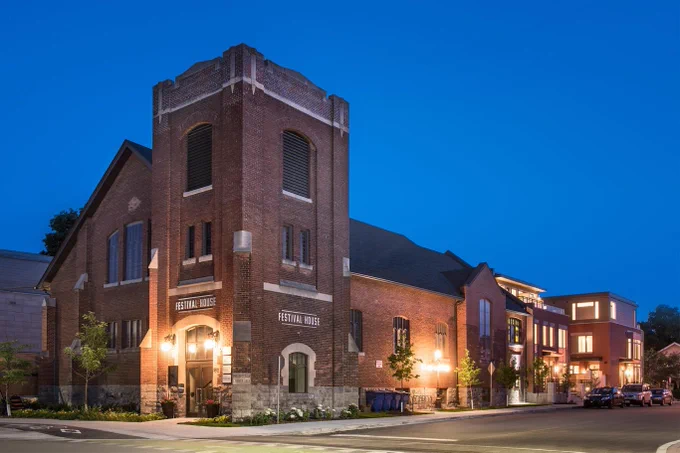 A red-brick Edwardian church lit up at dusk, infill development in the rear, with signage reading Festival House.