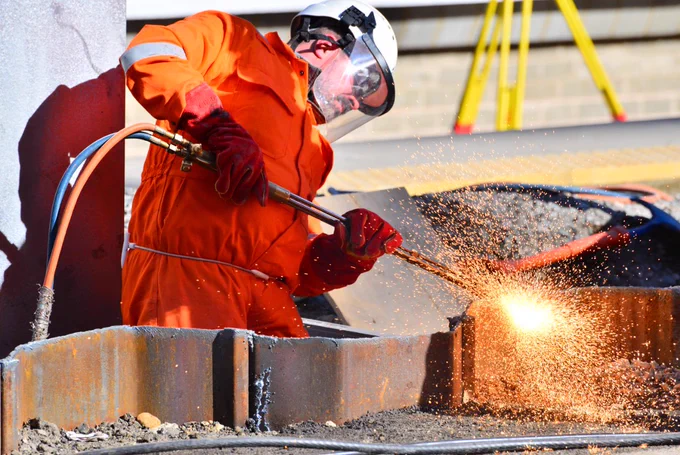 An engineer wearing a visor uses cutting equipment on a redundant piece of metal outside London King’s Cross station.