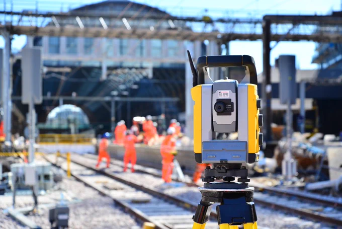 A photo of a theodolite being used by engineers, with London Kings Cross Station in soft focus in the background.
