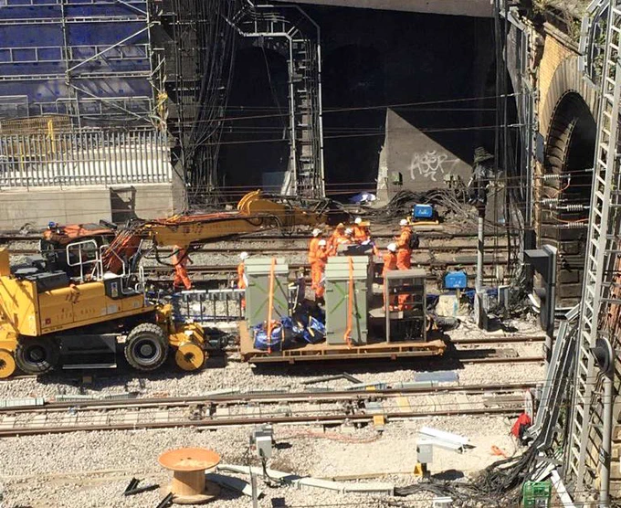 A crane pushes a large trolley carrying metal boxes, which will hold signalling equipment once installed, along the railway track into Gasworks Tunnel at London Kings Cross