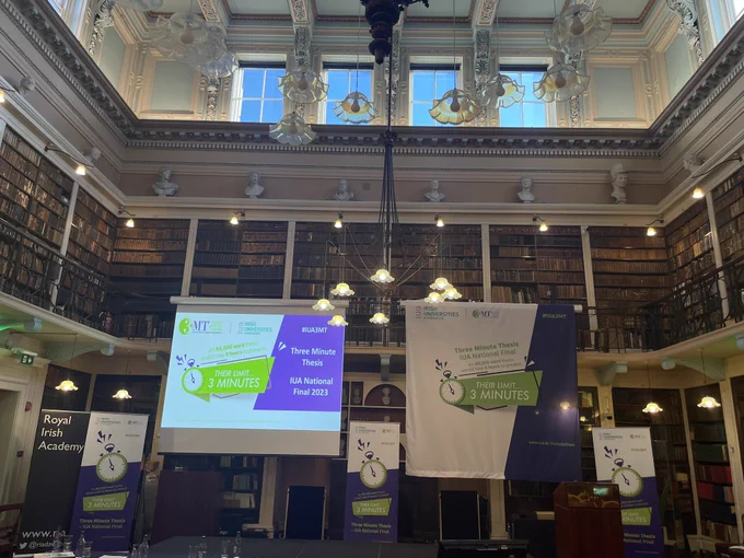 Stage in the RIA Dublin, with slide on projector screen reading Three Minute Thesis competition national final