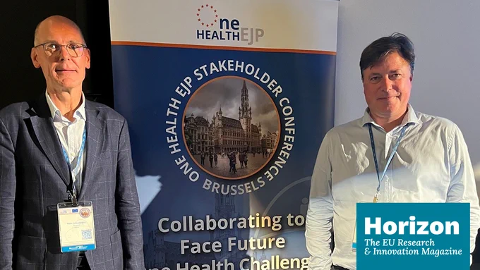 The two researchers standing in front of the One Health EU event roll-up banner and the Horizon Magazine logo at the bottom.