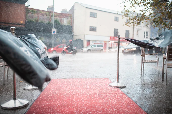 Photo of driving rain, hailstones, flooded pavement and canvases being whipped into the air by the wind.