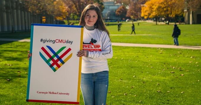 Image of CMU student holding the Giving CMU Day sign in front of Hunt Library.