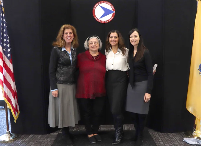 Four professionals stand in front of a black curtain with an American flag on the left side and smile at the camera