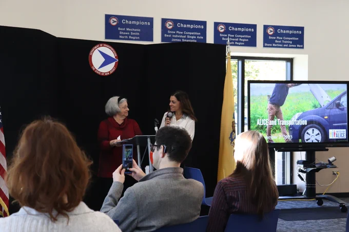 Diane Gutierrez-Scaccetti and Kiran Handa Gaudioso stand a a podium and smile at each other while an "ALICE and Transportation" presentation displays on a screen next to them