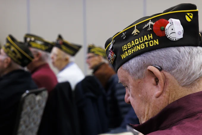 A veteran wearing a hat with "Issaquah, Washington" on it bows his head in reflection during a Veterans Day ceremony.
