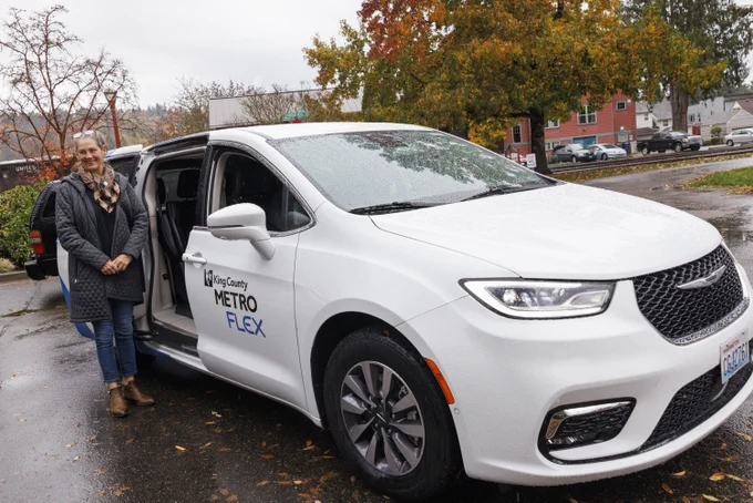 A smiling woman clasps her hands as she stands next to a white Metro Flex van, door open.