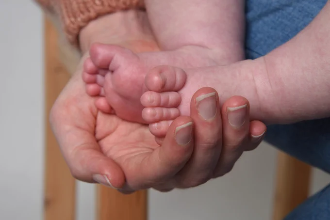 An adult hand holding two babies' feet