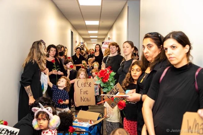 Parents and children in a hallway, wearing mostly black and holding signs and flowers