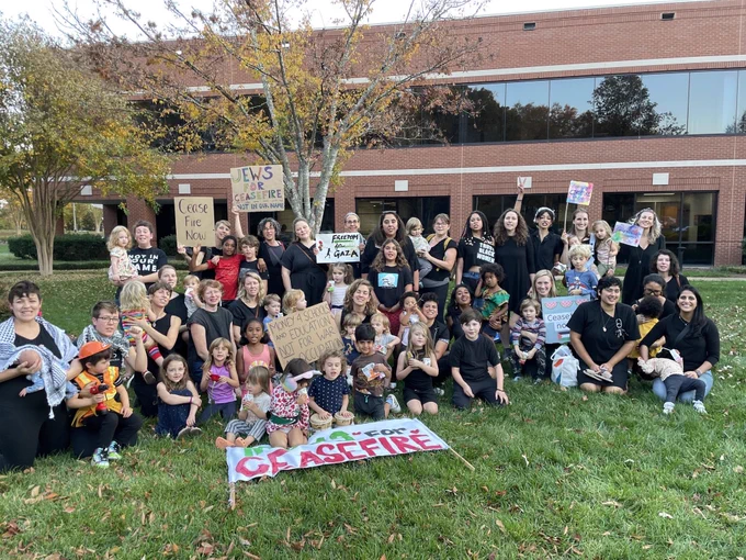Large group of parents and children sitting and standing on grass with a range of signs calling for a ceasefire
