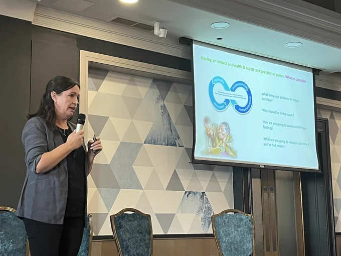 Women on stage with a slide talking about the what help to have an impact