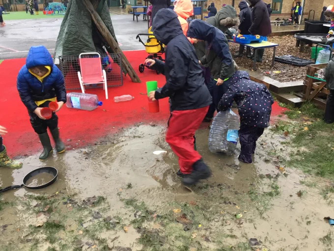 Children using lots of different containers to transport muddy water around during a rainy playtime.