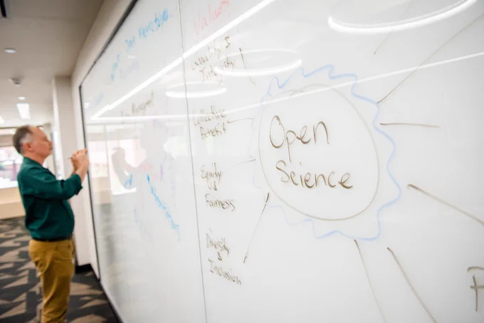 Person writing on a whiteboard in the background with "Open Science" written in the foreground
