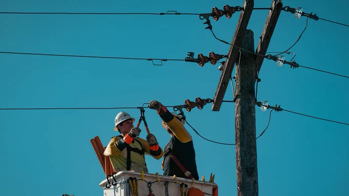 Workers wearing safety gear doing electrical work on power lines at height.