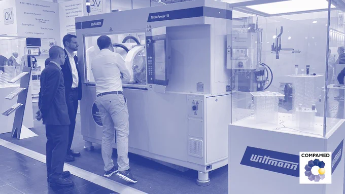 Image: Three men are standing in front of a large production machine at an exhibition stand; next to it are two display cases with materials and products.; Copyright: beta-web | Messe Düsseldorf