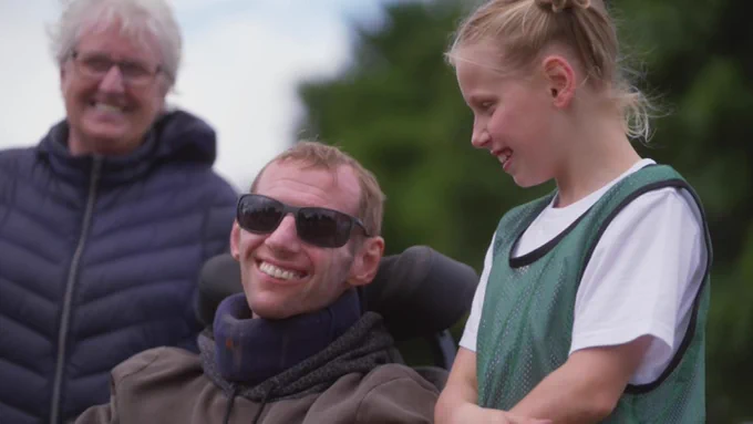 Rob Burrow wears sunglasses and smiles as he sits outdoors