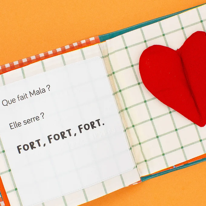 que fait mala ? elle serre ? fort, fort, fort. l'illustration est un coeur rouge avec deux matières a toucher et serrer sur un tissu à carreaux